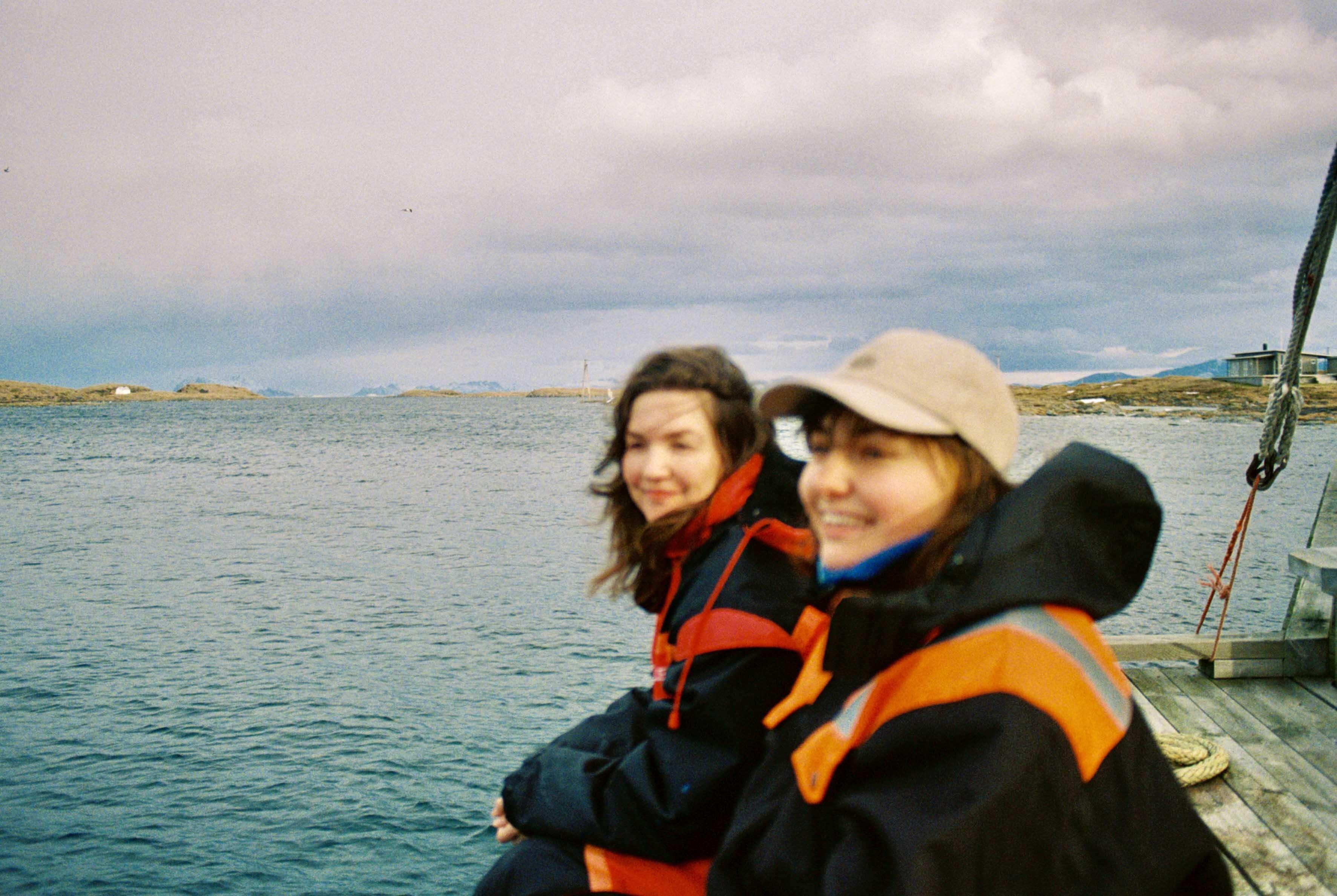 To jenter i oljehyre står på en brygge og ser utover sjøen.