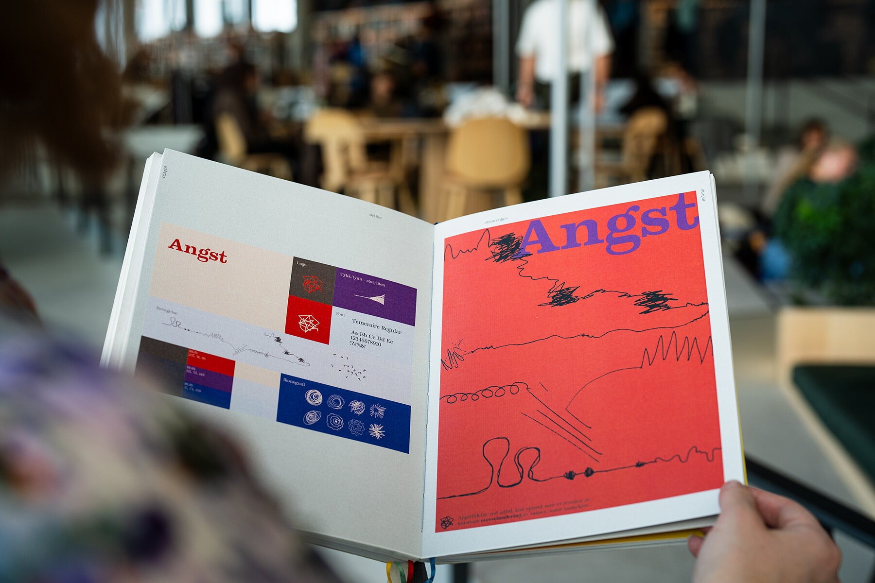 Hender som holder en bok åpen. Sidene viser typografi og andre grafiske elementer.