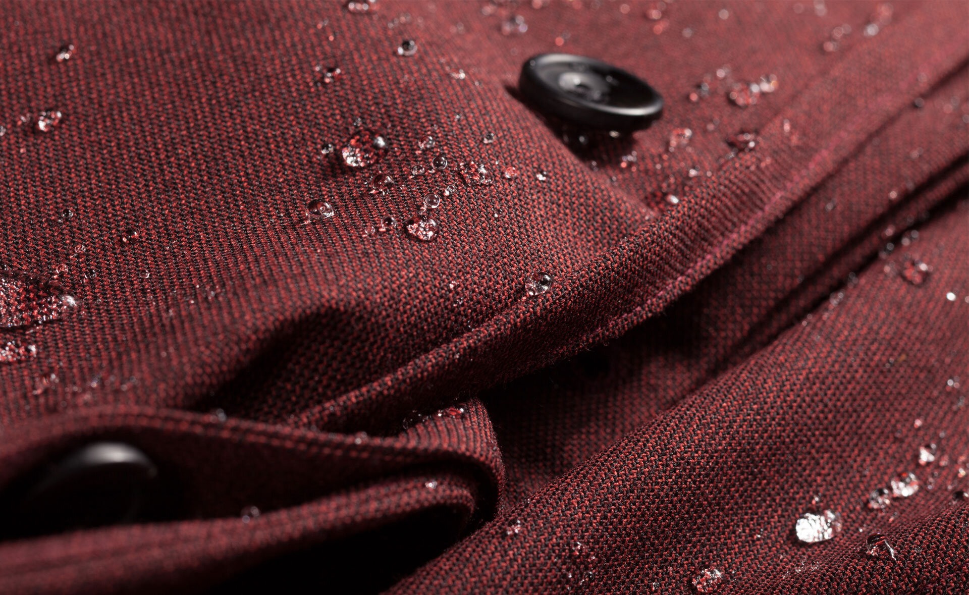 Nærbilde av et ytterplagg i burgunder, med regndråper.