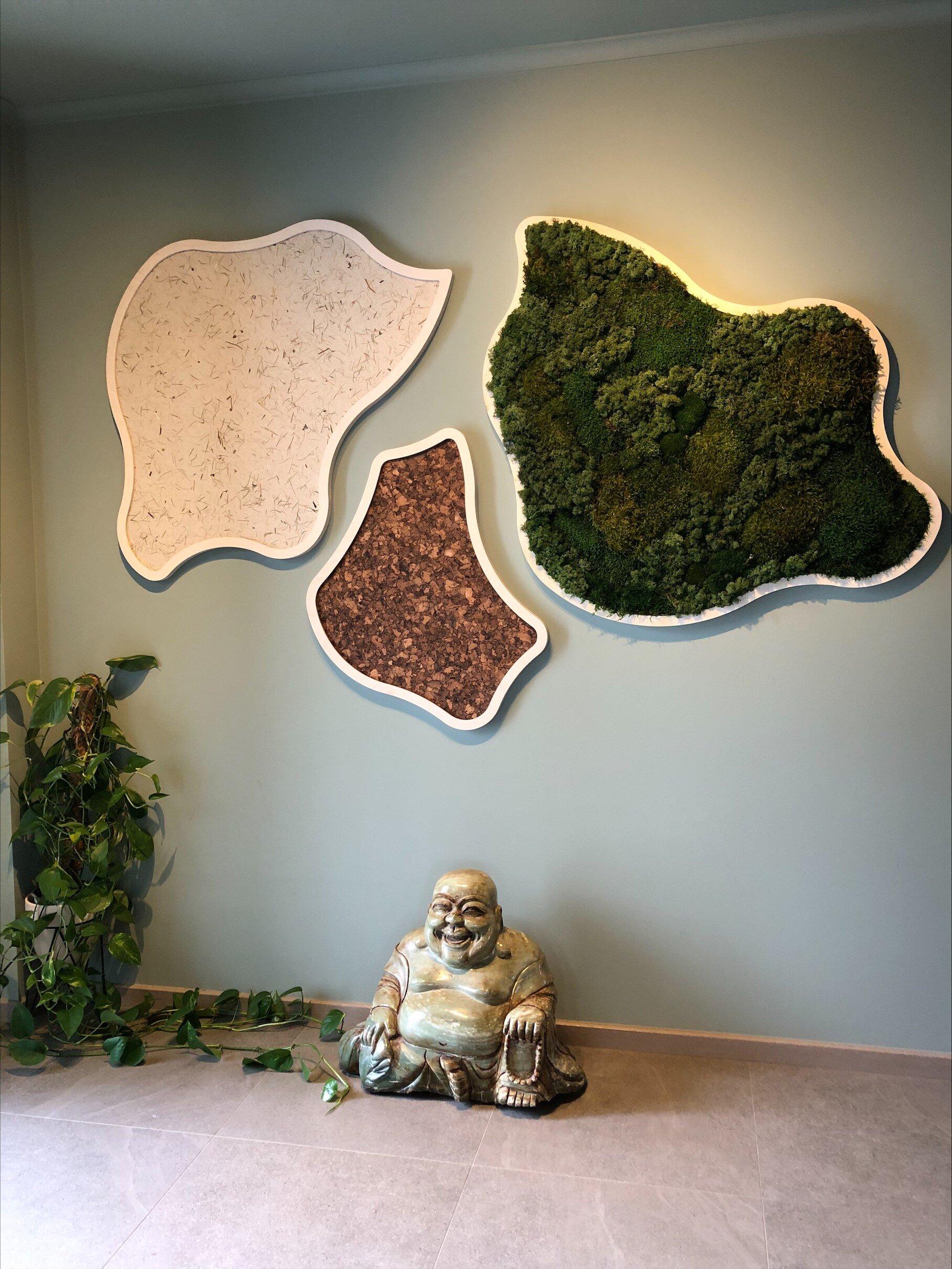 Vegg med tre organiske paneler i naturmaterialer, inkludert mose, og en Buddha-figur unde.