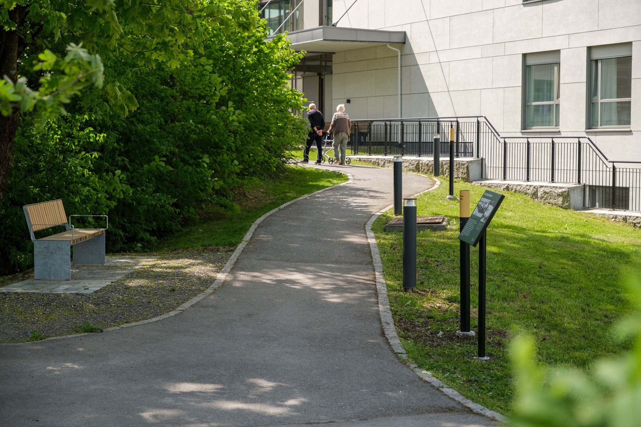 To eldre personer går tur på minnestien: en bred, asfaltert sti gjennom en park.