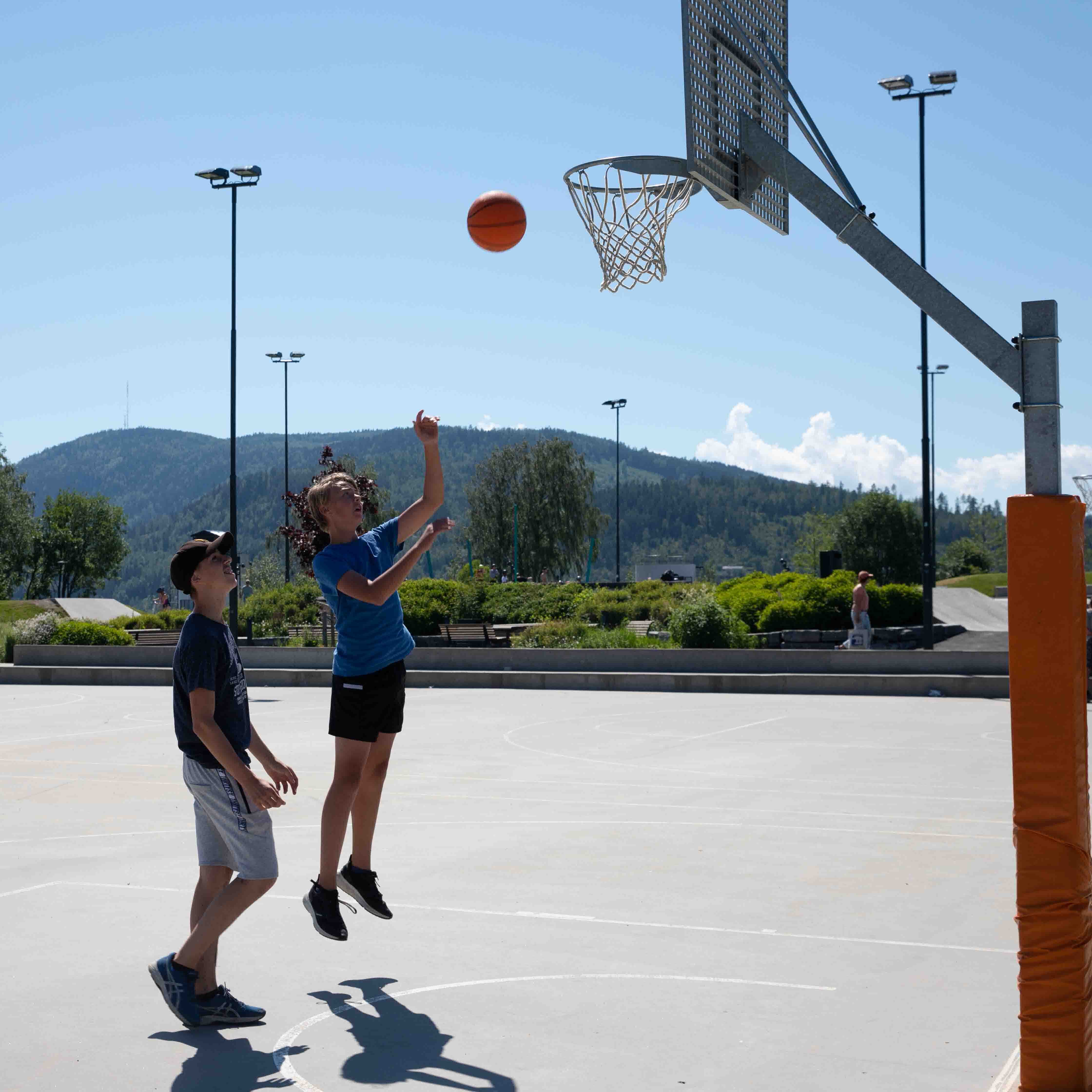 To gutter som spiller basket. Ballen er på vei opp mot nettet.