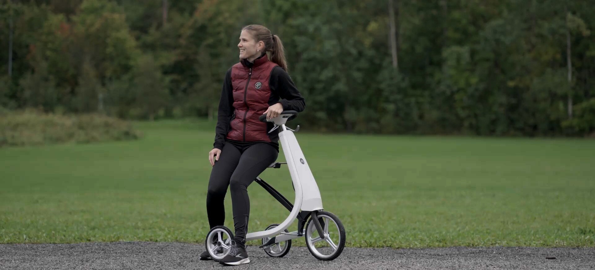 Kvinne i rød vest sitter på en Movu med gress rundt.