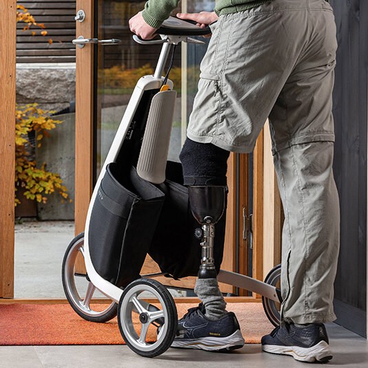 Underkroppen på en mann med benprotese. Han står og holder i styret på en Movu trehjuling.