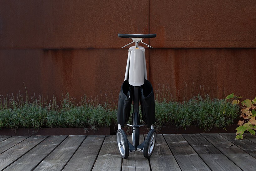 Hvit trehjuling Movu, sett fremfra mot rustrød vegg.