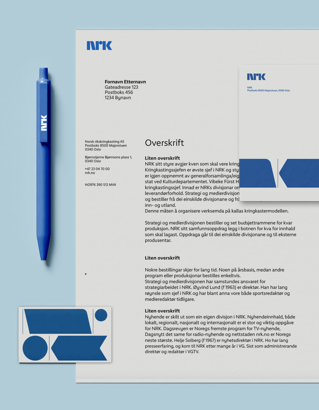 NRK brevpapir, konvolutt, penn og visittkort mot lys blå bakgrunn. Logo på papiret er i mellomblå.