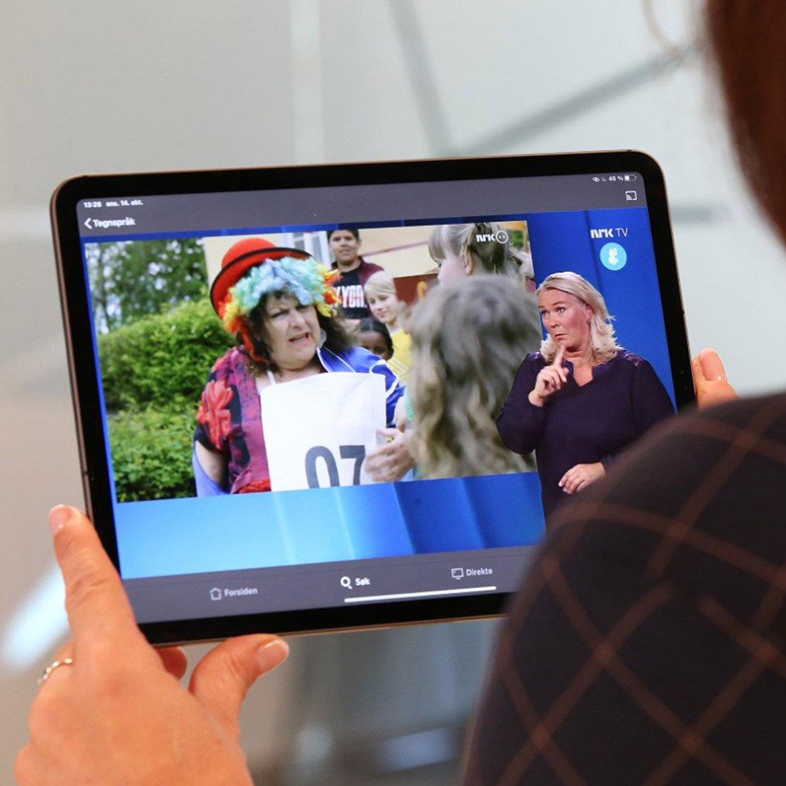 Nærbilde av en person som holder et neddbrett. På nettbrettet spiller en tv-serie med tegnspråktolk.