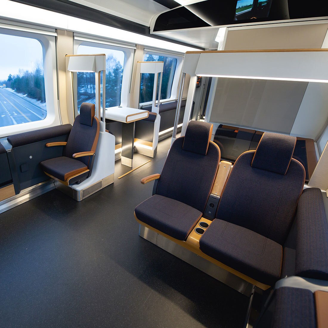 Interiørfoto fra flytoget viser ulike seter og sitteløsninger: polstrede seter med nedfellbare armlener, ti i par på en side og ett enslig på motsatt side av midtgangen. Bak det enslige setet er en seksjon med to "barstoler" rundt et høyt bord.