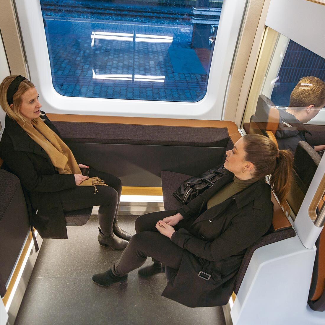 To kvinner sitter overfor hverandre på hvert sitt nedfellbare sete på Flytoget.