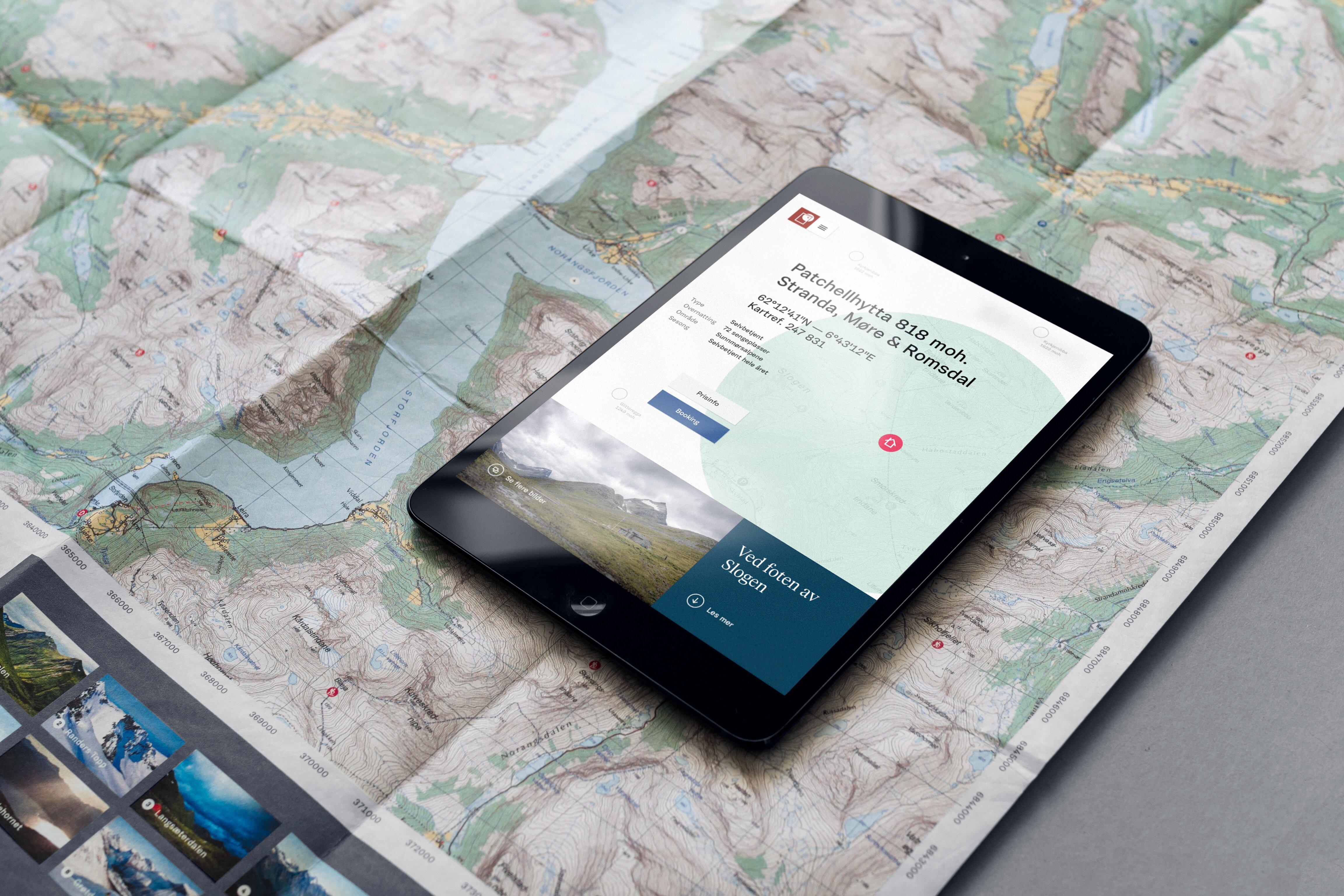 Bildet viser en ipad som ligger oppå et utbrettet analogt kart. På skjermen ses informasjon om en turisthytte i det aktuelle området.