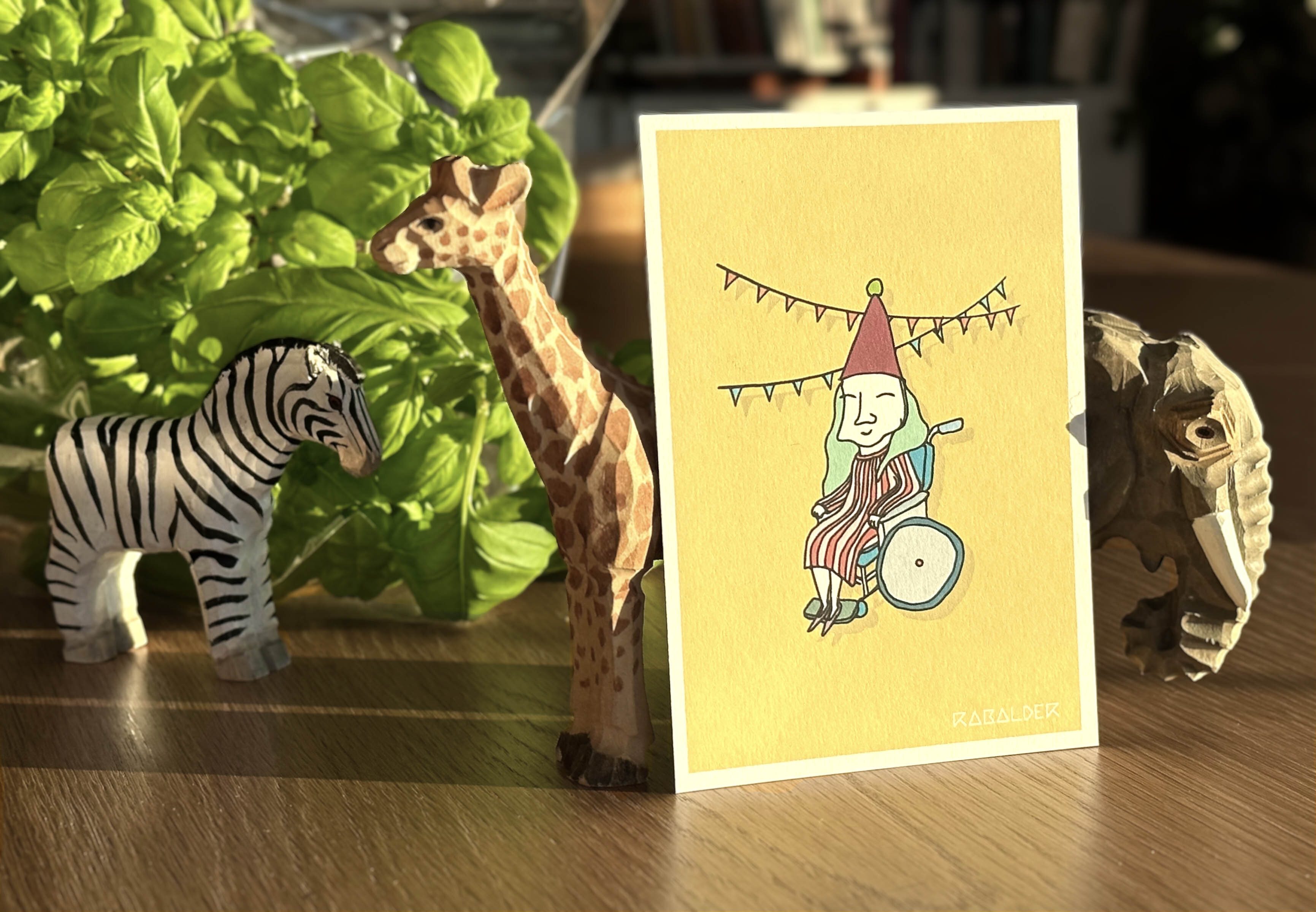 Illustrert gratulasjonskort med dame i rullestol og bursdagshatt på hodet.