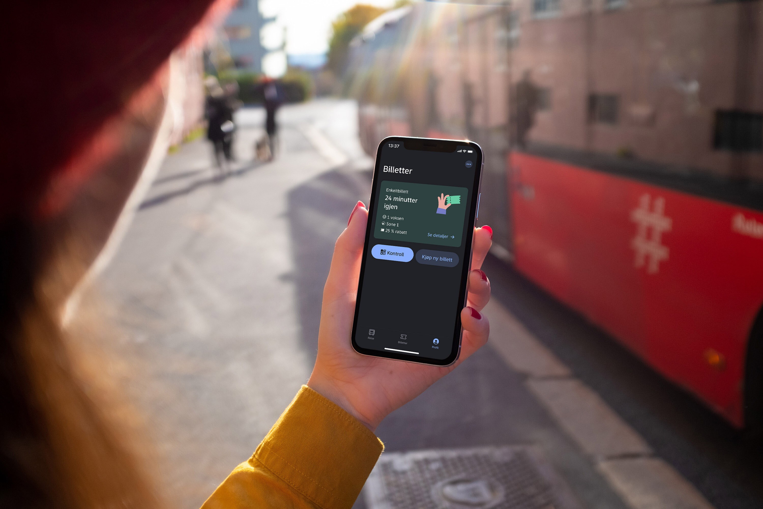 En person holder en mobil med Ruter-appen på skjermen, med en rød trikk i bakgrunnen.