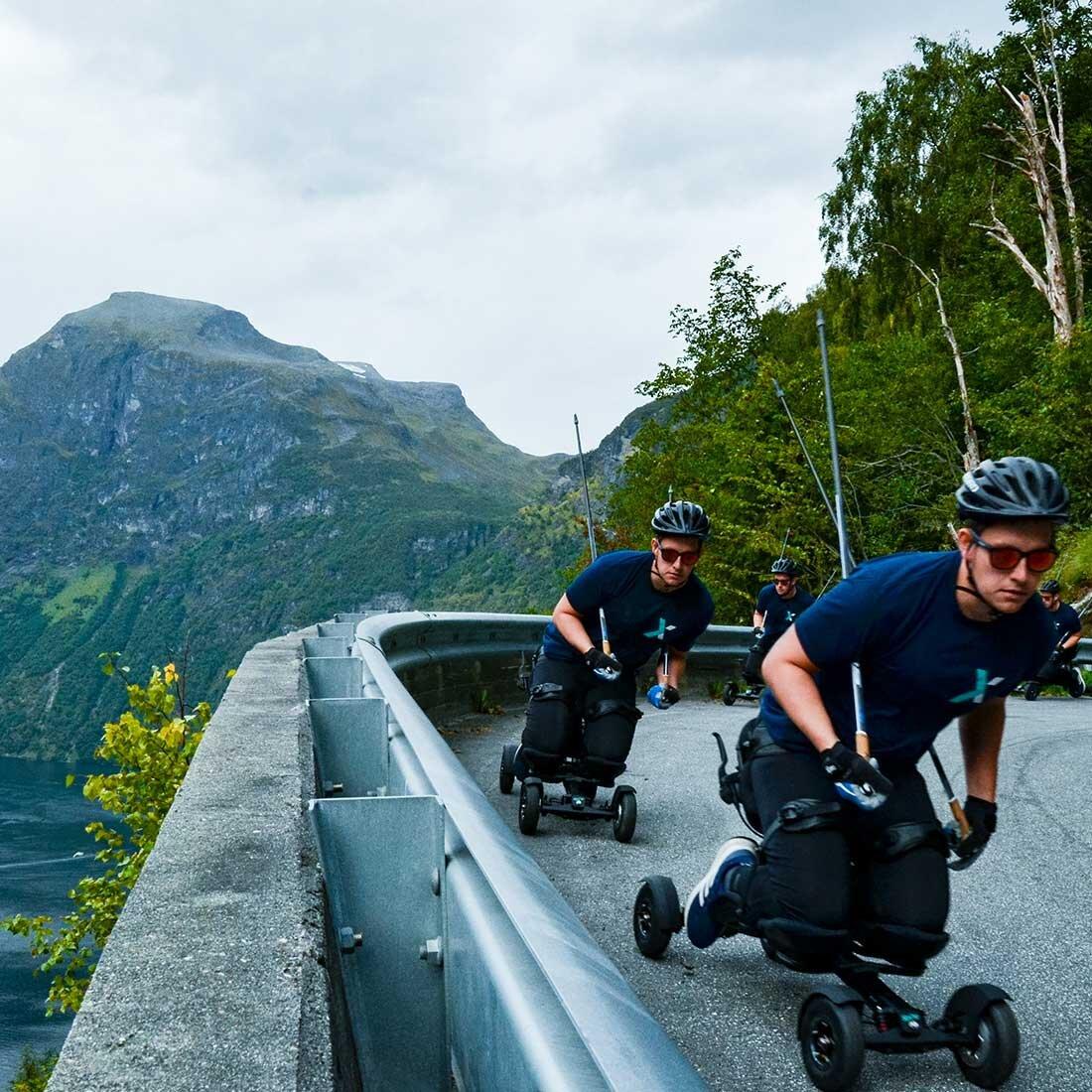 En montasje viser en person i flere kopier som kjører spike gjennom en sving på en landevei i et vakkert fjordlandskap.