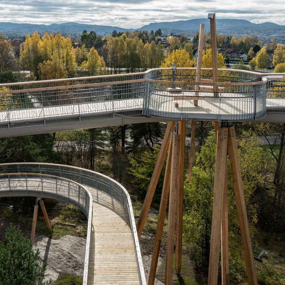 En møteplass i løypen er støttet av et titalls massive trebjelker. Det er sittemøbler, trekledd platting og gelender i stål med håndløper i treverk.