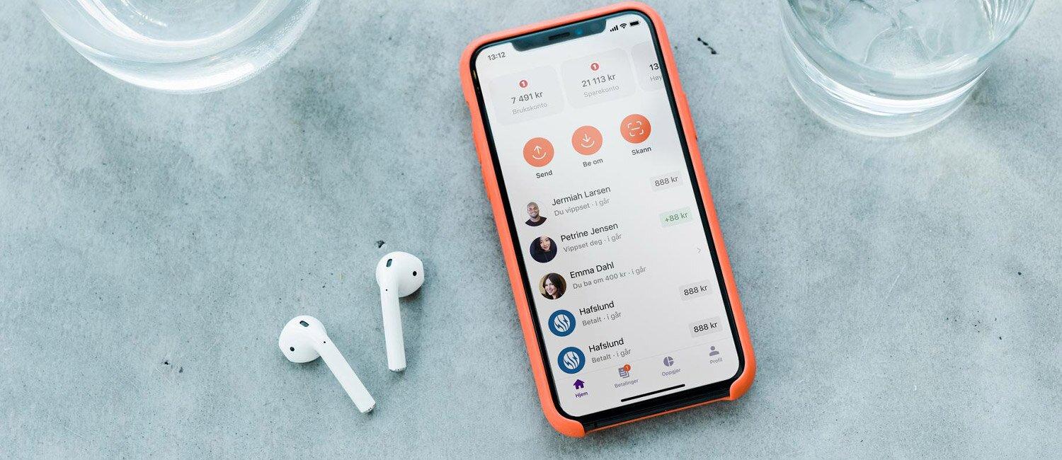 En smarttelefon på et bord, med Vipps-appen åpen. Landingssiden viser hurtigknapper for å sende og be om penger – og skanne qr-kode, samt en liste over nylig aktivitet.