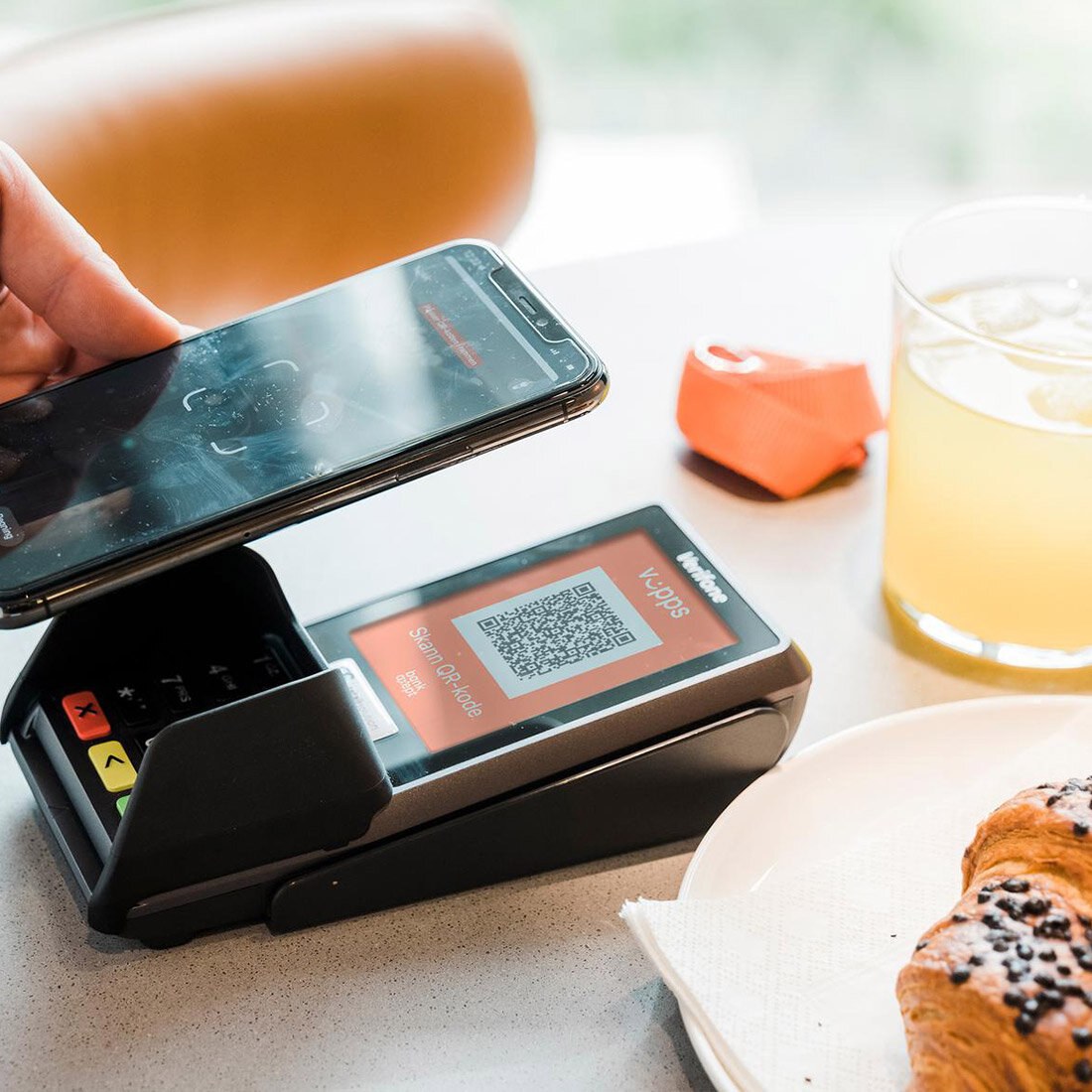 Nærbilde av en smarttelefon som scanner en Vipps-QR-kode på en betalingsterminal – i en kafésetting.