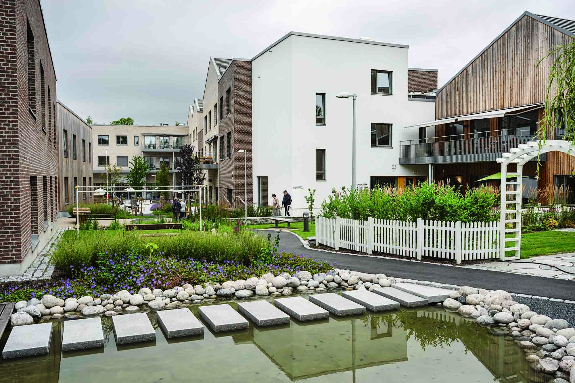 Uterom med asfalterte gangstier og beplantning omgitt av bygg.