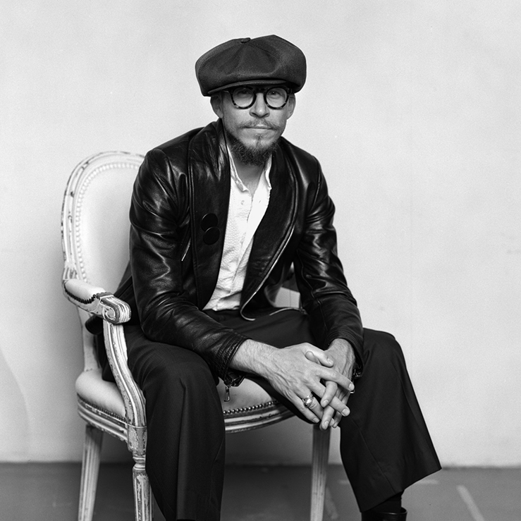 Svart-hvitt-portrett av Alexander Helle i skinnjakke, sittende på en antikk stol med sixpence.