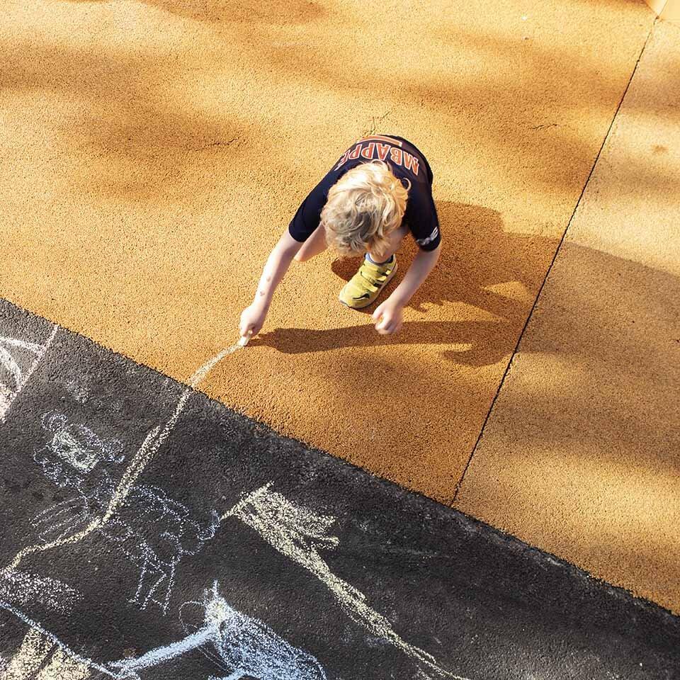 Et barn sitter på huk og tegner på bakken med kritt.