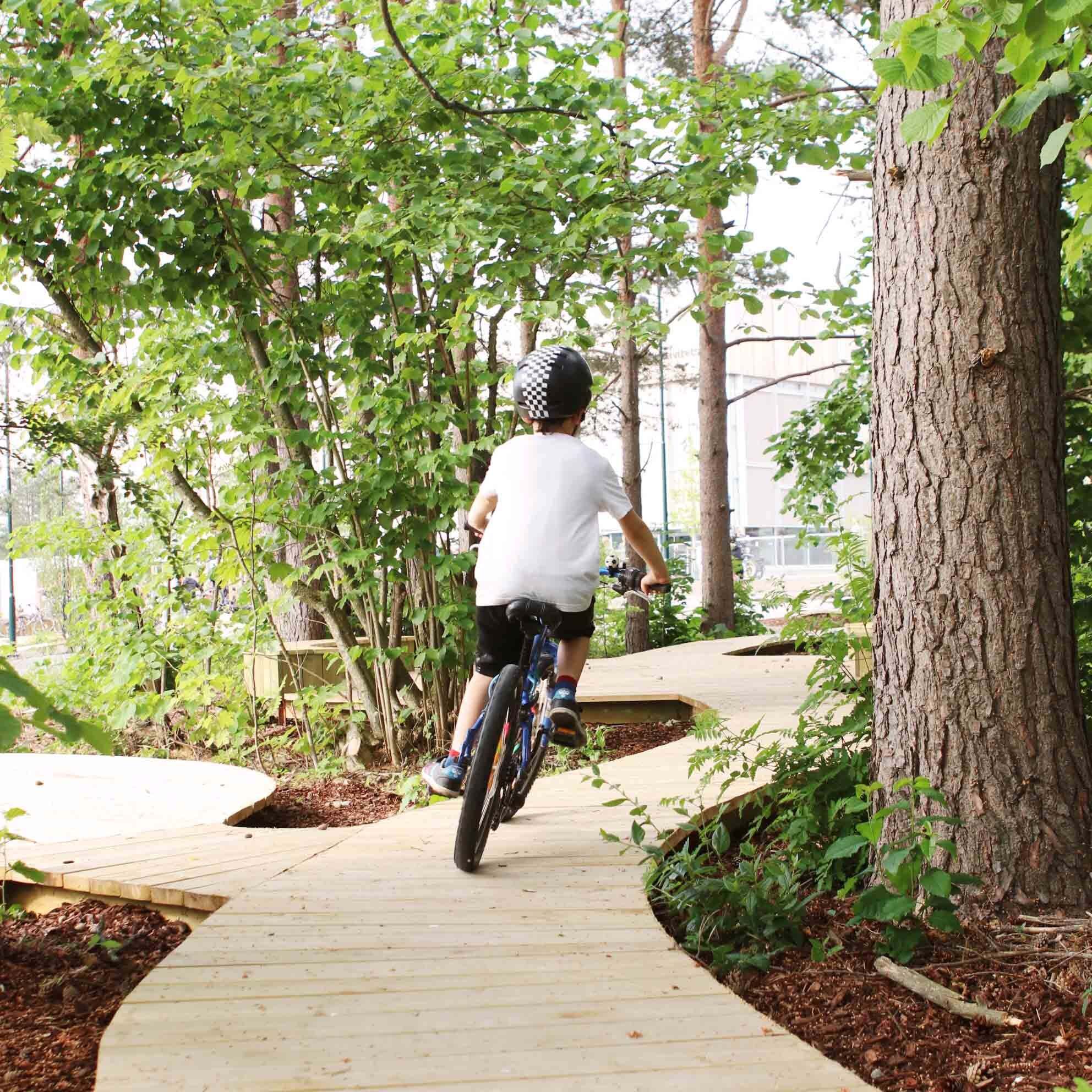 Ryggen til en gutt som sykler på en sykkelsti av treplanker.