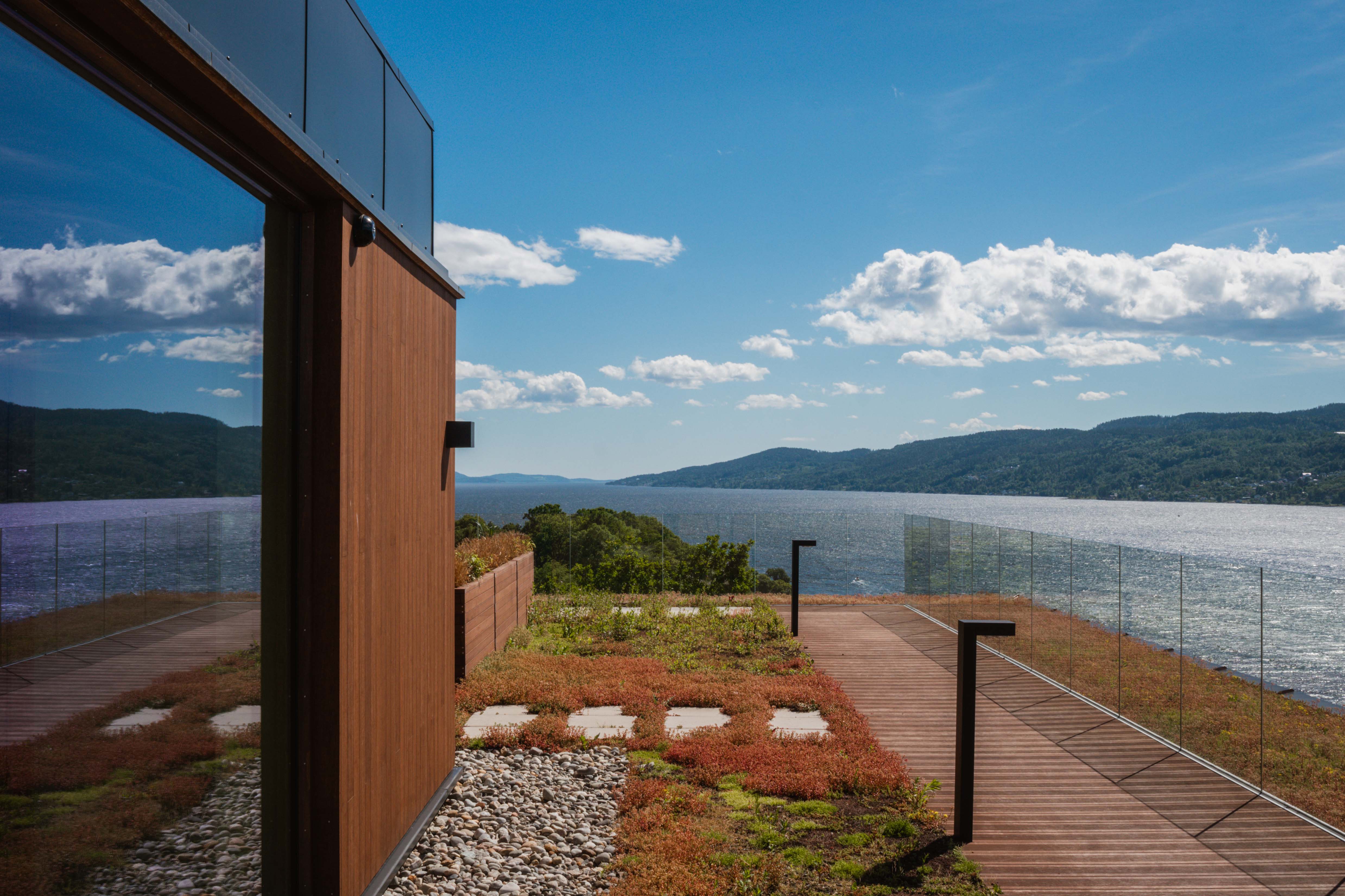 Foto av en takterrasse med store glassfasader, dekke av sedum og utvikt over fjord og åser.