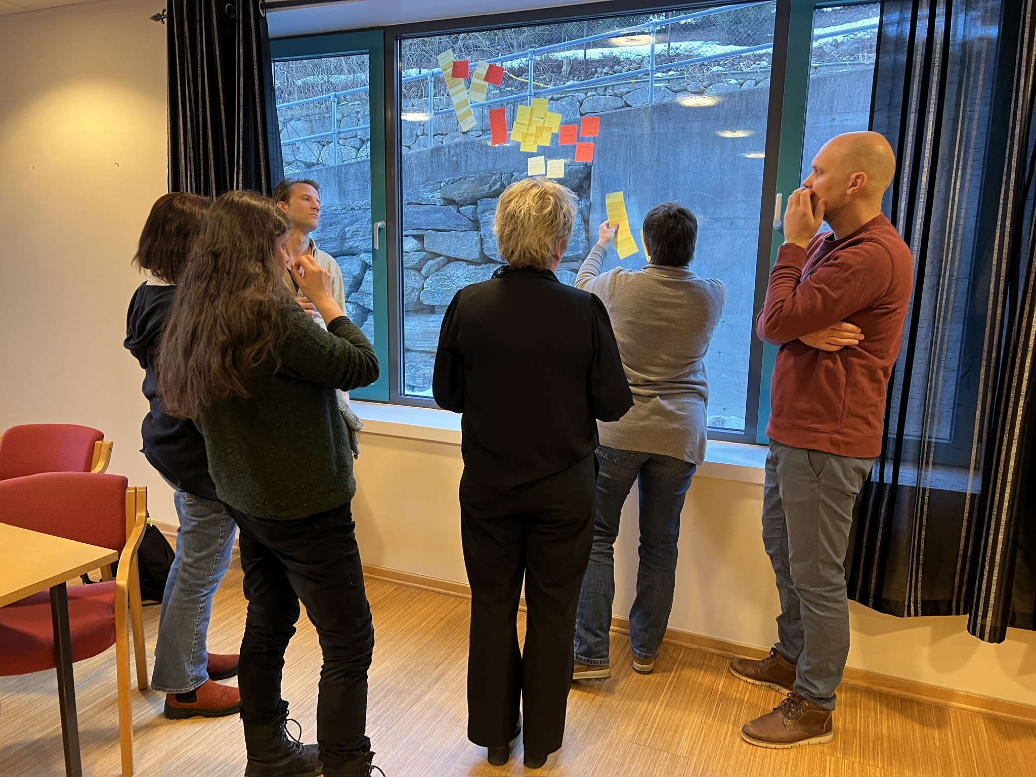 En gruppe mennesker står og ser på et vindu der det er klistret opp post-it-lapper i ulike farger.