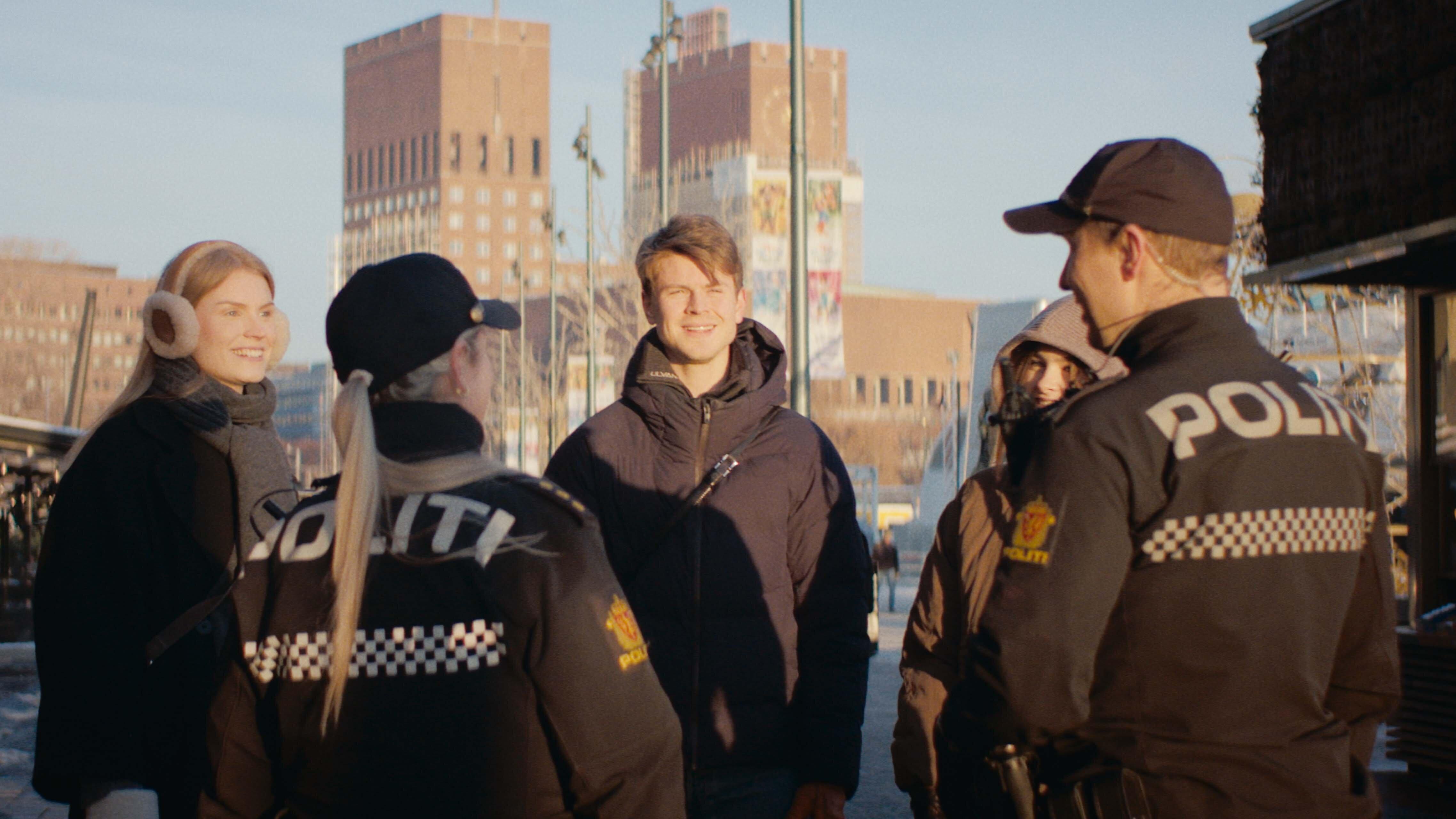 To politikonstabler prater med tre unge mennesker som smiler. Rådhuset i Oslo skimtes i bakgrunnen.