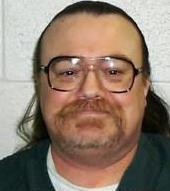 A middle-aged white man with large rimmed glasses, long hair, a mustache, and a beard.