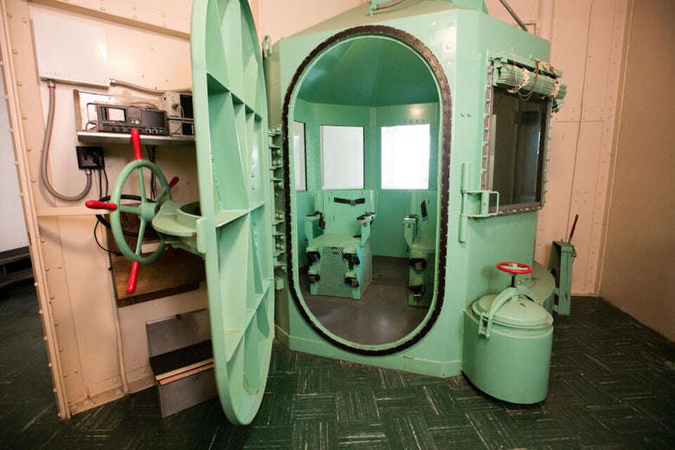 A bright green metal chamber with an open oval door. A chair and windows are visible inside.
