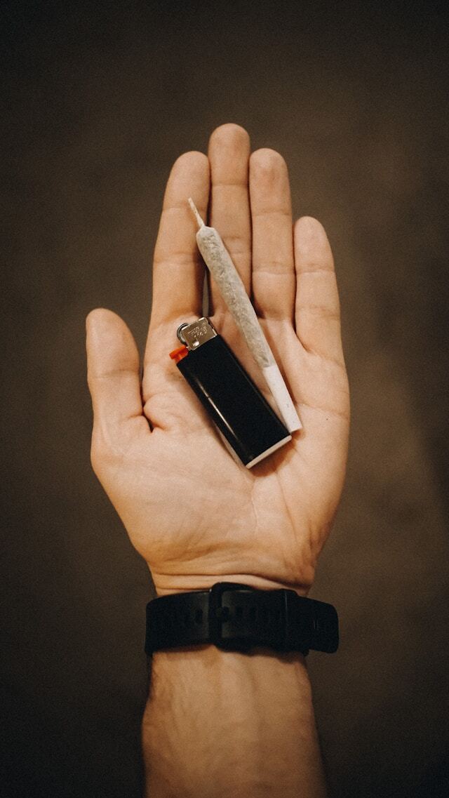 Person holding out a hand with a lighter and joint.