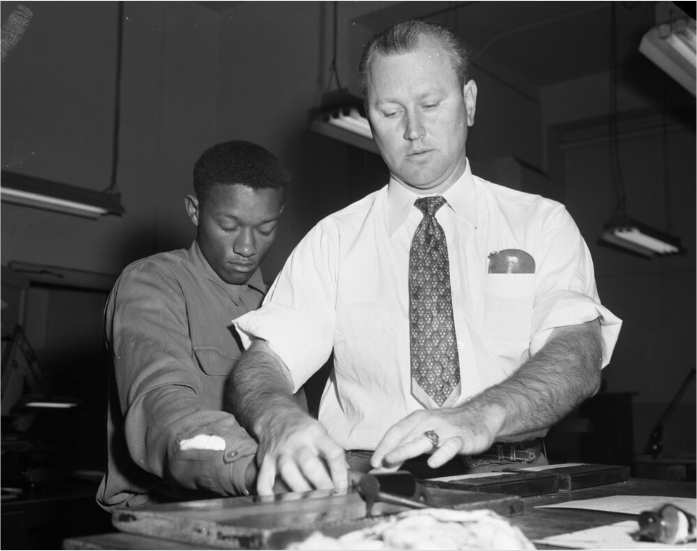 Tommy Lee Walker, a young Black man, looking down and closing his eyes as he is fingerprinted by a white man in a tie.