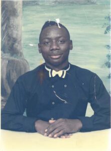 Warren King, a young Black man wearing a black double-breasted button-down shirt and a white bowtie with black stripes in front of an illustrated nature backdrop