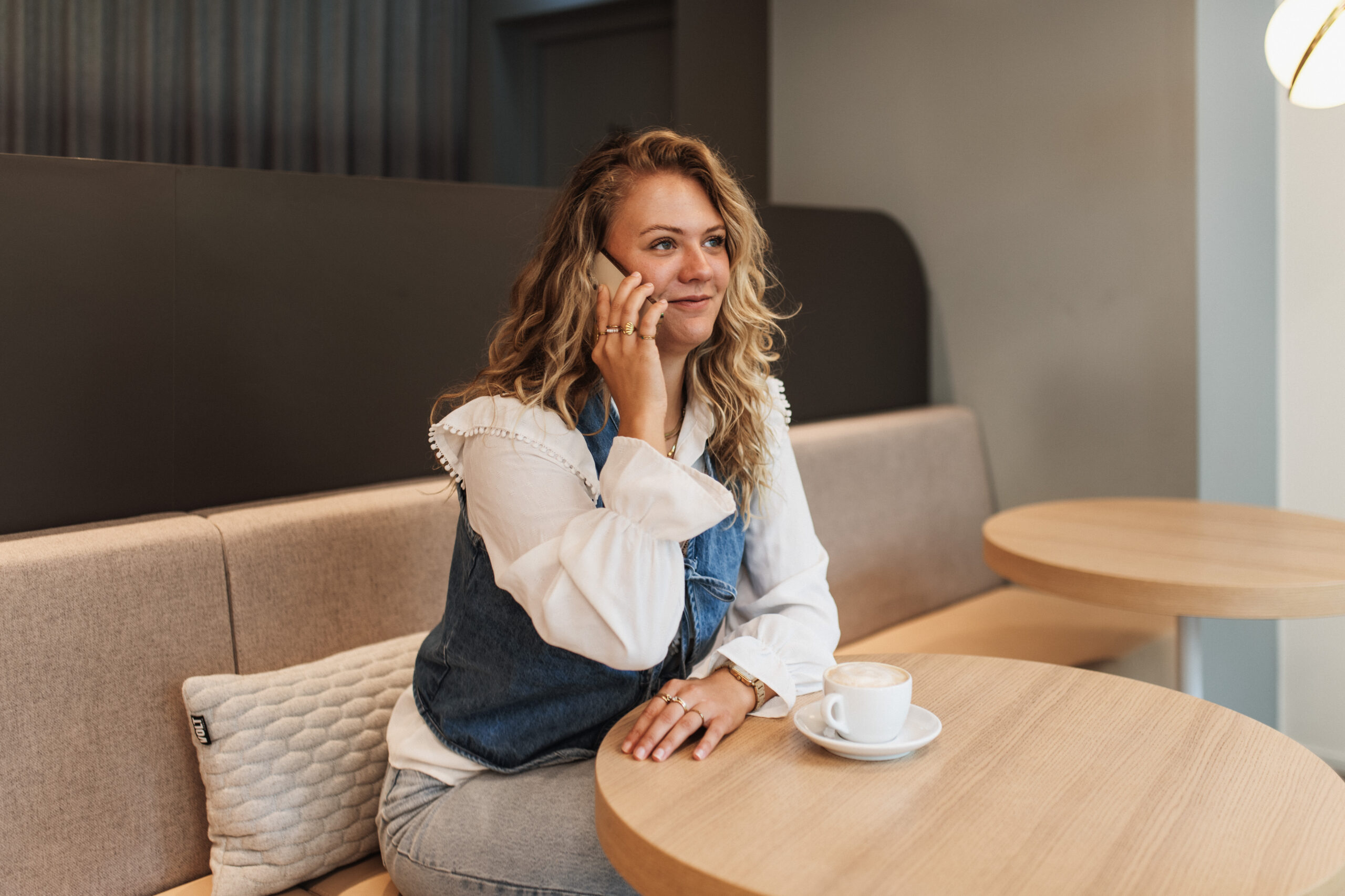 Woman with curly hair sitting in a sofa in an office space with a computer