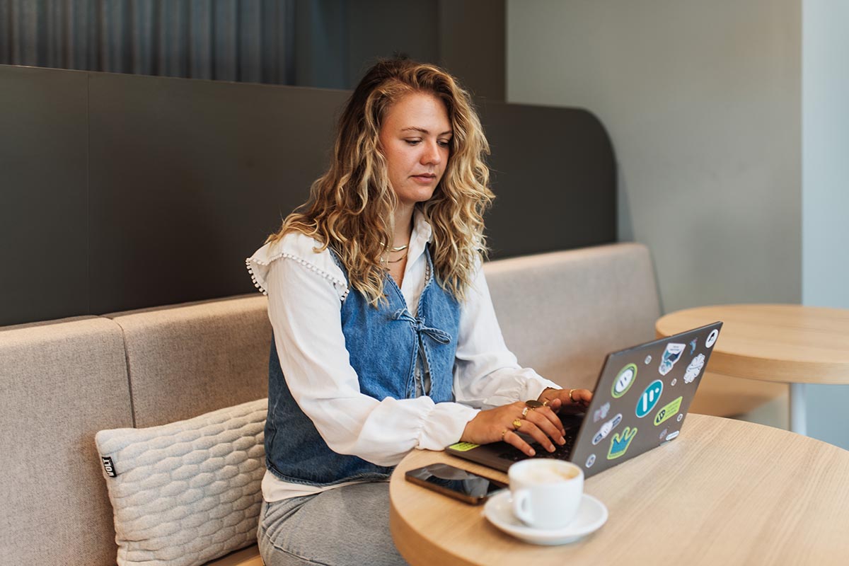 a woman works on a laptop sitting in a booth at a cafe