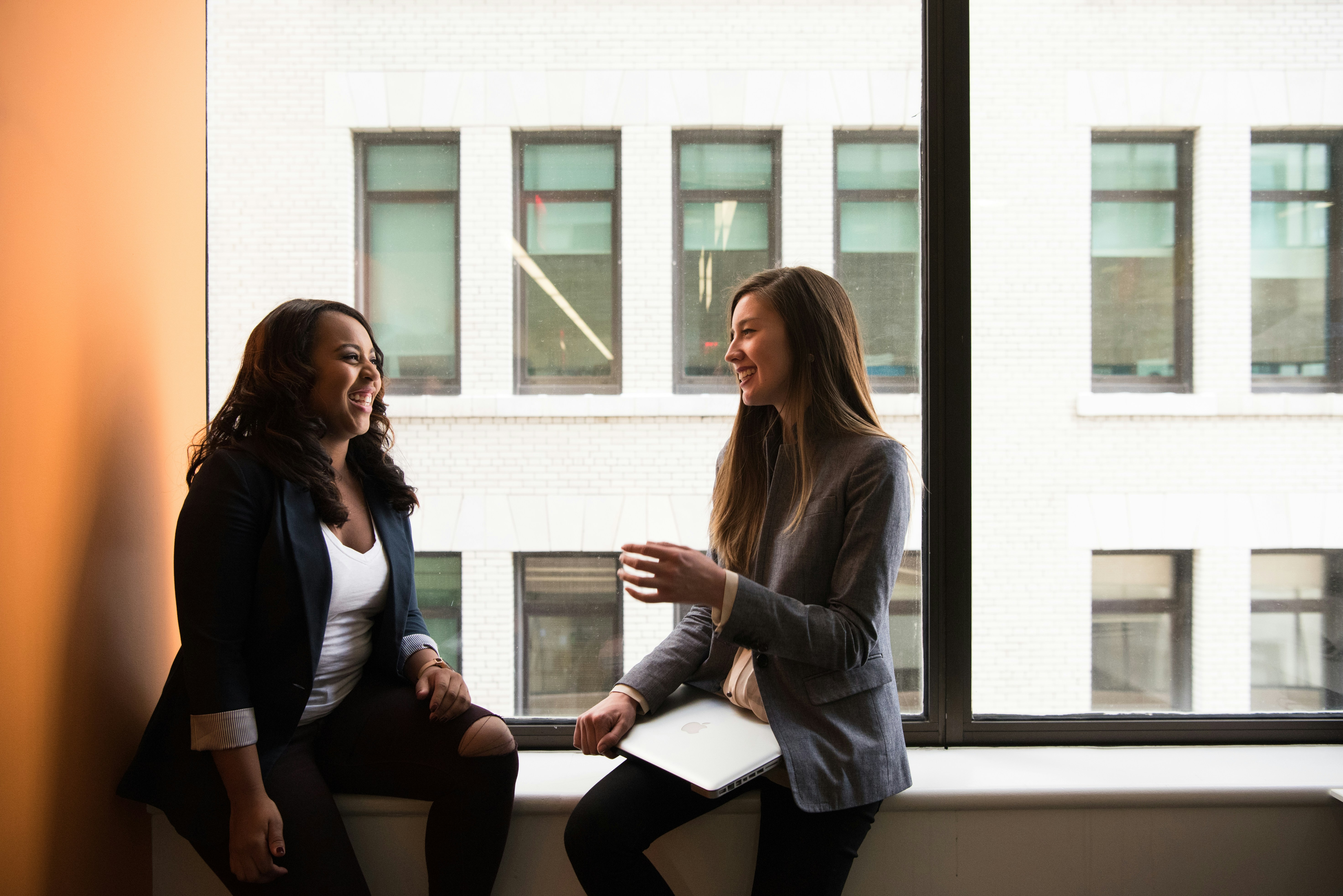Two happy women sitting in a window discussing.