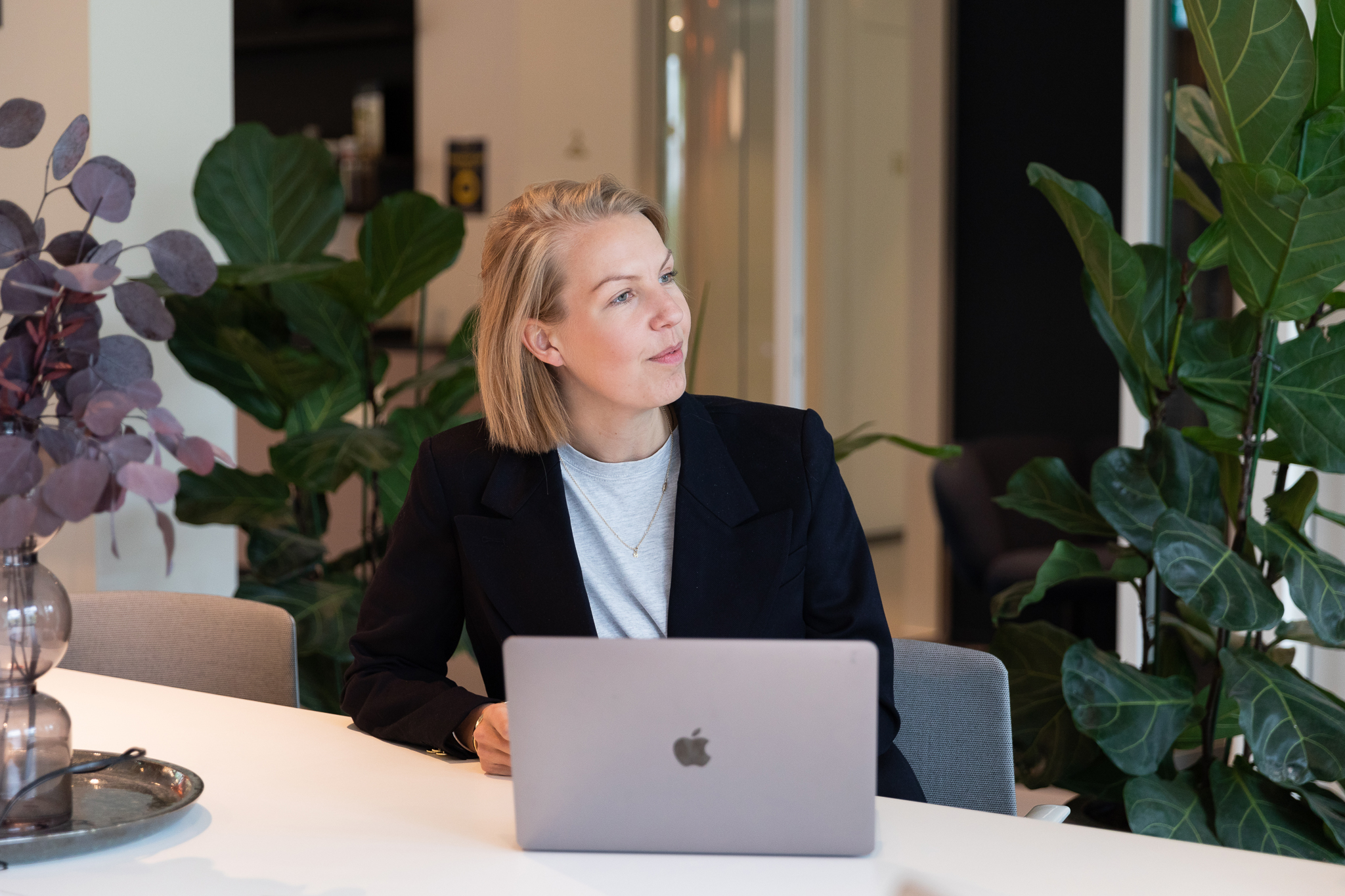 Woman sitting at a white table having an Apple computer in front of her in an office enviroment.