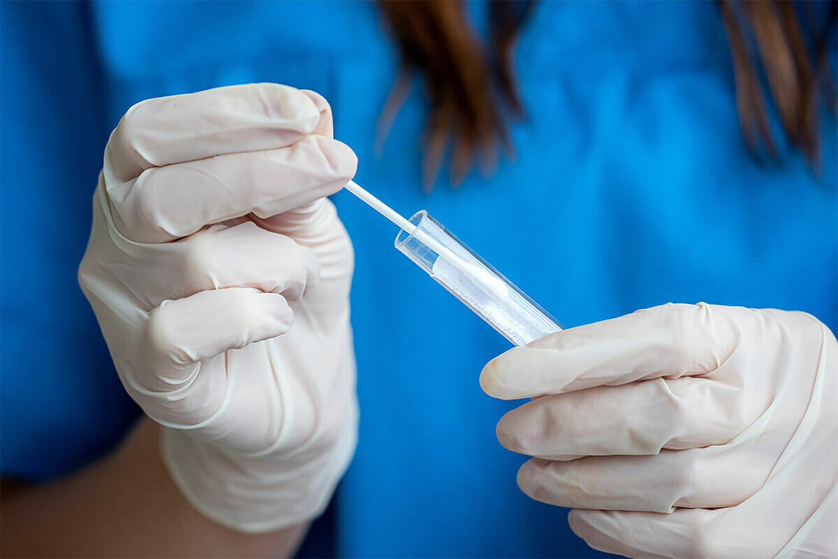 Medical Technician putting a swab of oral fluid into a test tube