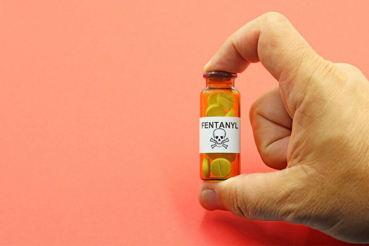 Hand holding a brown vial filled with pills labeled Fentanyl with a skull and crossbones