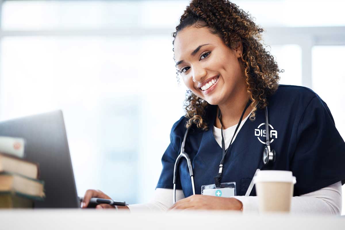 Nurse sitting at a desk and smiling, wearing DISA scrubs