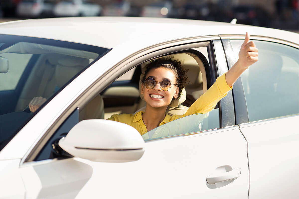 cheerful woman with sunglasses driving with thumbs-up