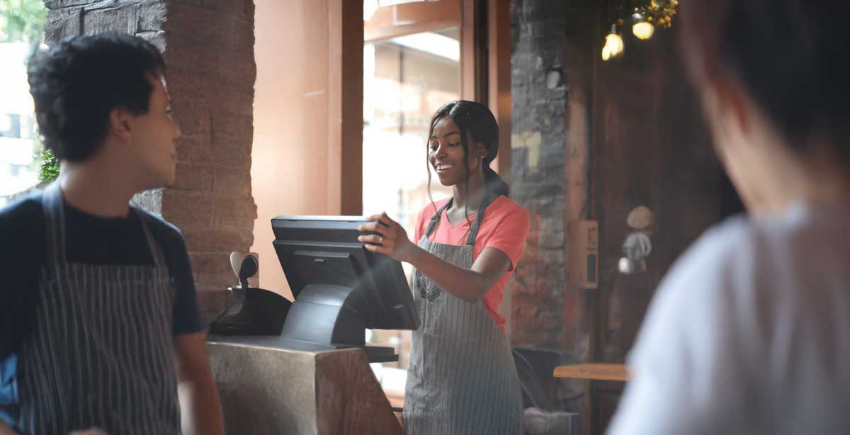 Young woman wearing an apron and operating a register at a cafe