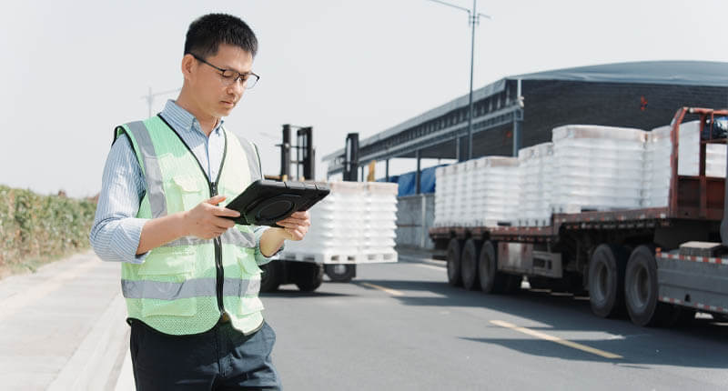 Logistics worker in safety vest using tablet to inspect cargo on truck at distribution center