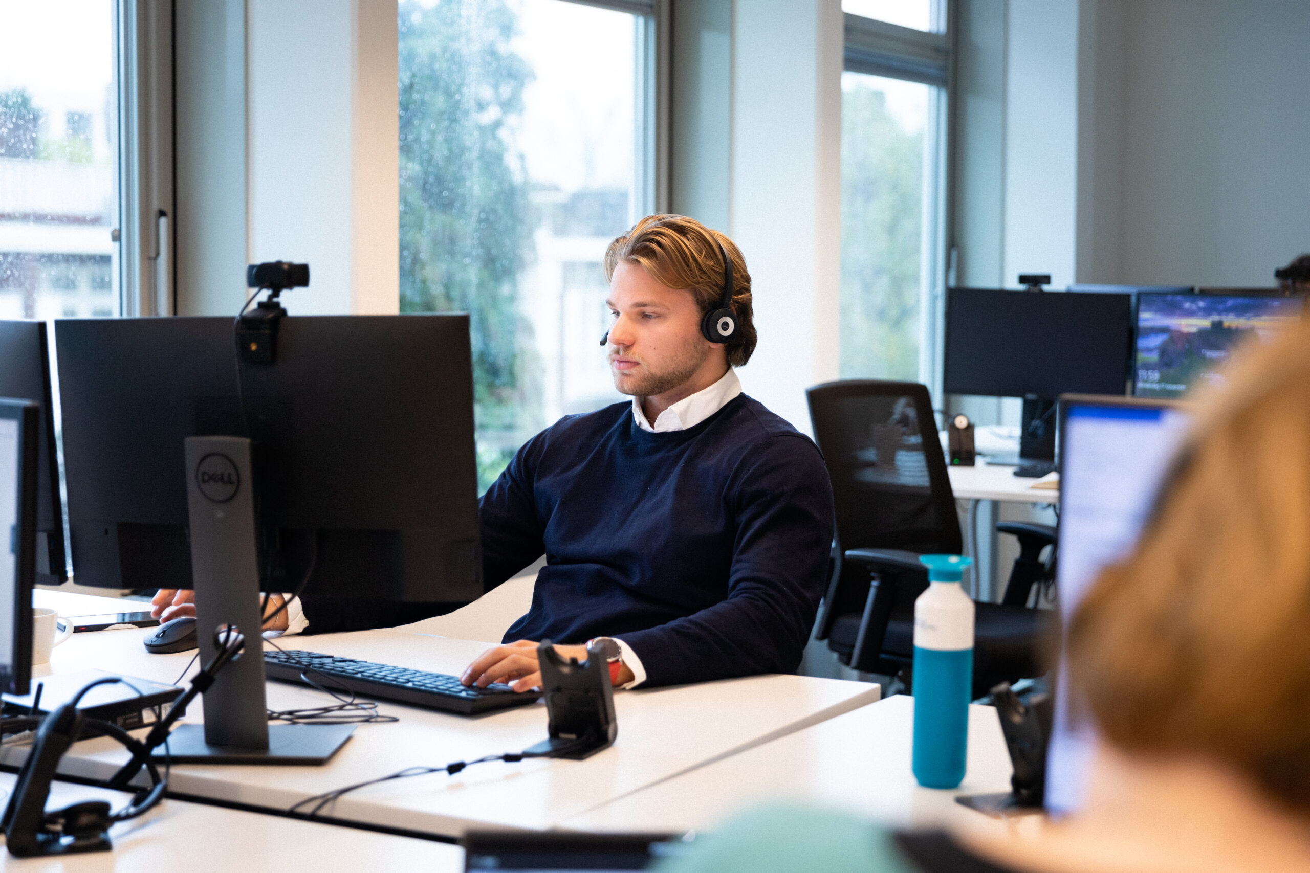 Kantoormedewerker met een headset die op een computer werkt