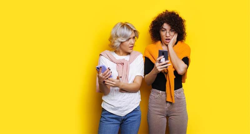 girl looking shocked at her mobile while posing near her friend