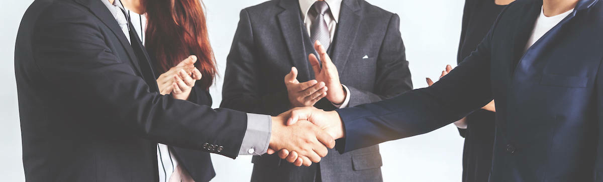 business people shaking hands while others clap