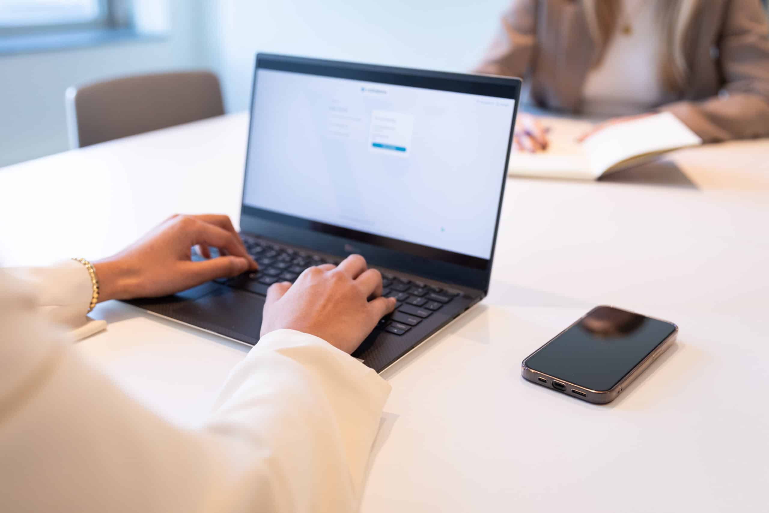 candidate sitting at desk while recruiter enters data on laptop