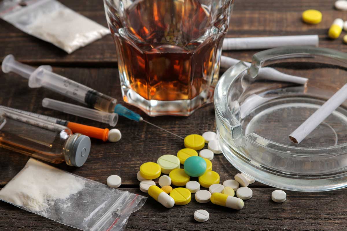 Various addictive drugs including alcohol, cigarettes, and drugs on a brown wooden table. Drug test