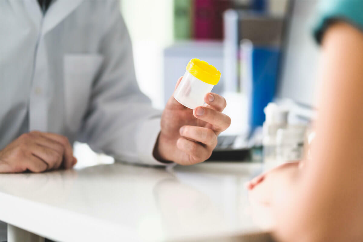 medical technician handing an empty urine specimen cup to a patient