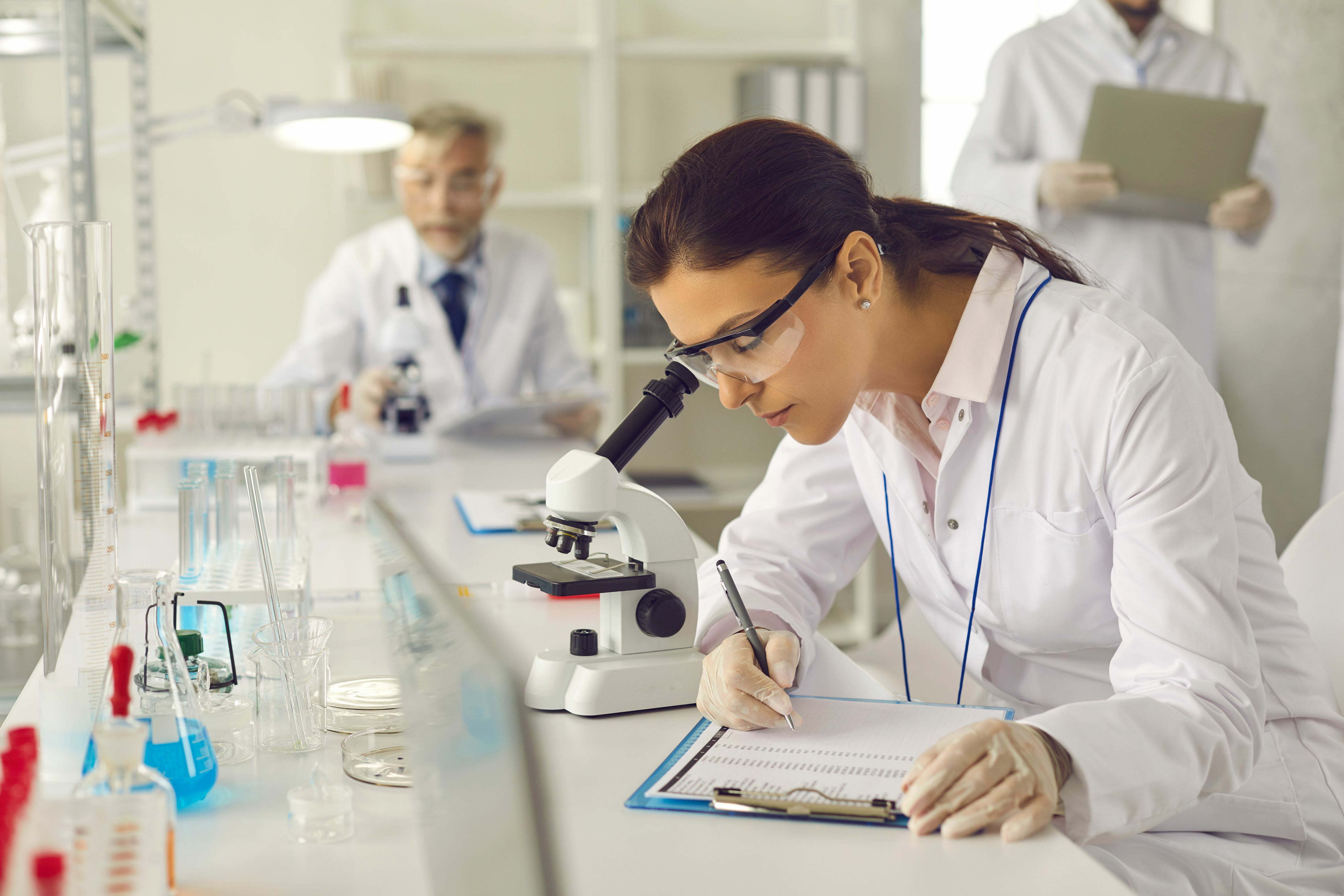 female scientist taking notes at microscope