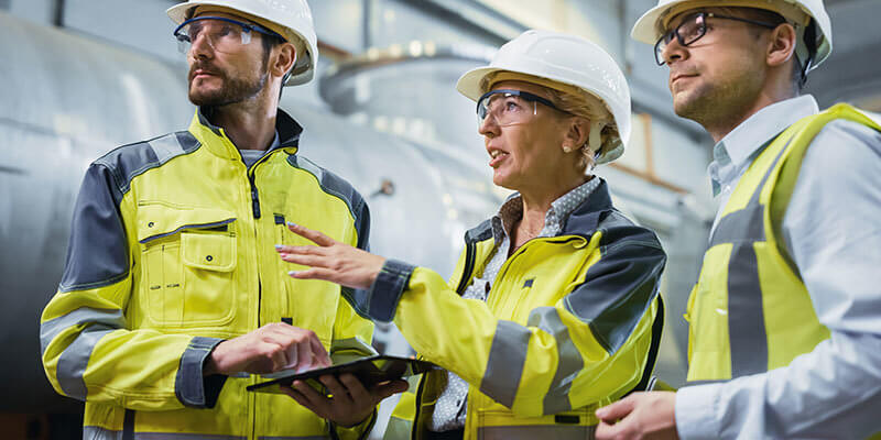Industrial worker wearing hard hats and safety vests having an onsite meeting